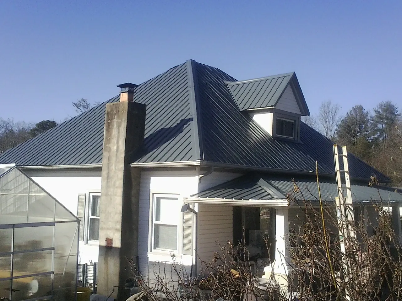 Dark blue standing seam metal roof on a white farmhouse with dormer — Slate & Tile Roof Repair by Roofing Brothers in Needville