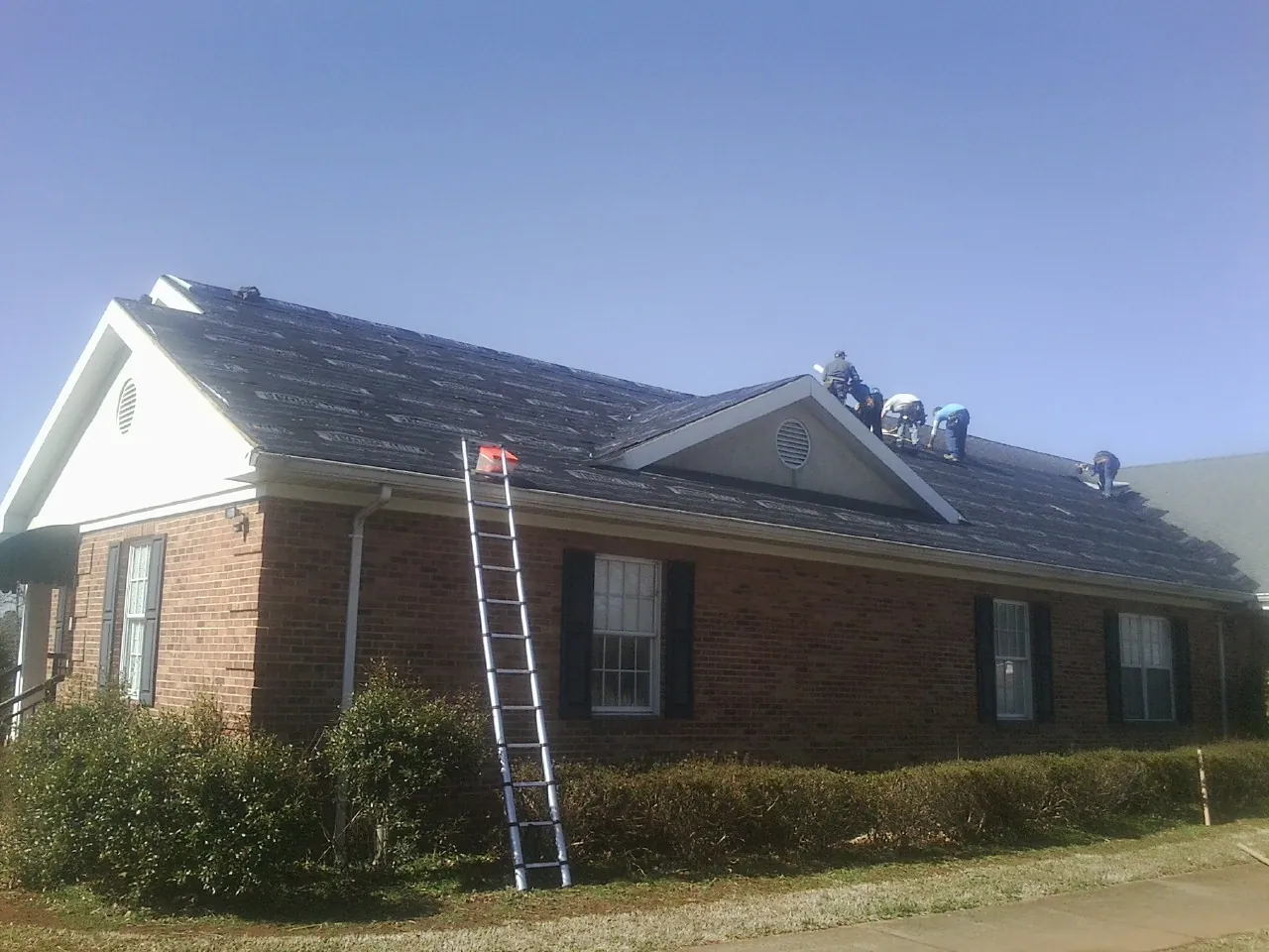 Crew tearing shingles off a brick ranch roof with a ladder set — Emergency Roof Repair work by our crew in Needville