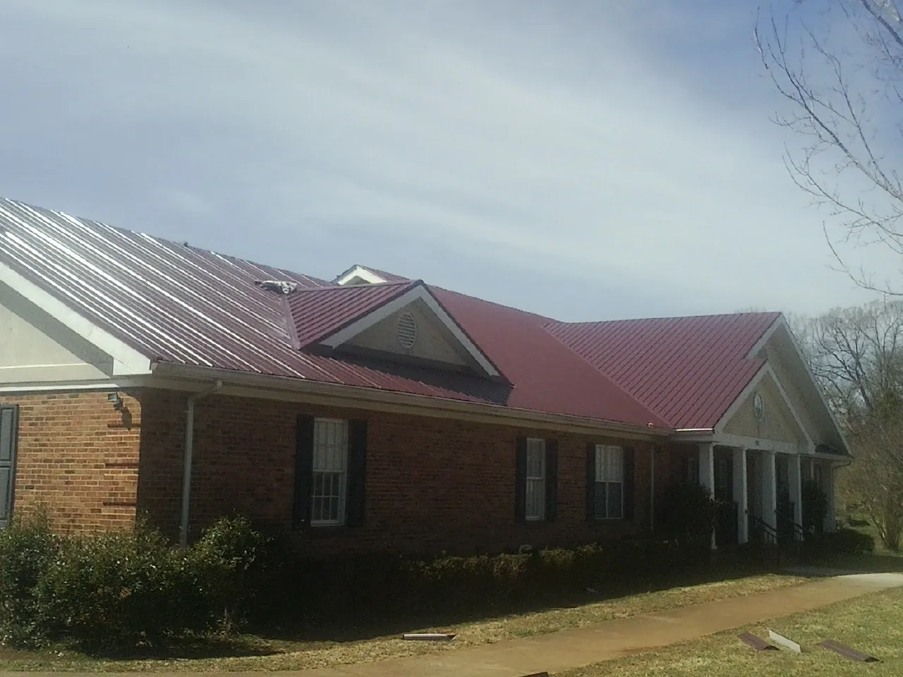 Red metal roof with gabled entries on a long brick building, from a Hail Damage Roof Repair job in Needville