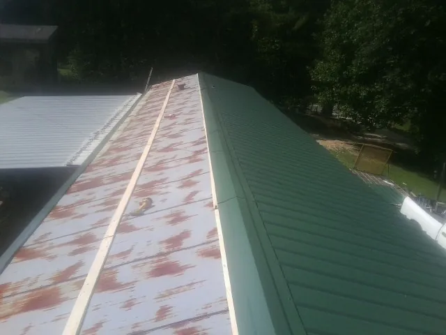 Old rusted panels beside newly installed green metal roofing — Wind Damage Roof Repair by Roofing Brothers in Needville