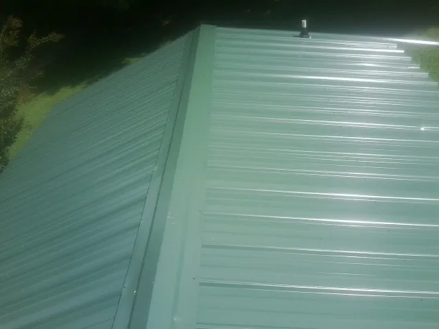 New green metal panels meeting at the ridge of a roof — Flat Roof Repair work by our crew in Needville