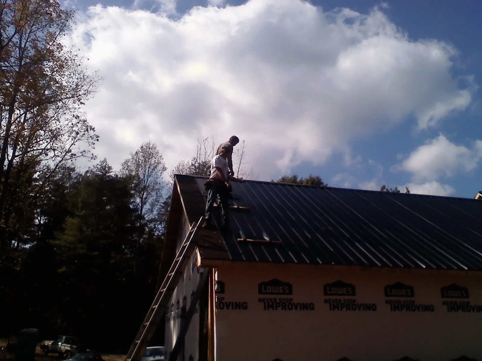 Roofer fastening dark metal panels high against a cloudy sky, from a Roof Inspection job in Needville