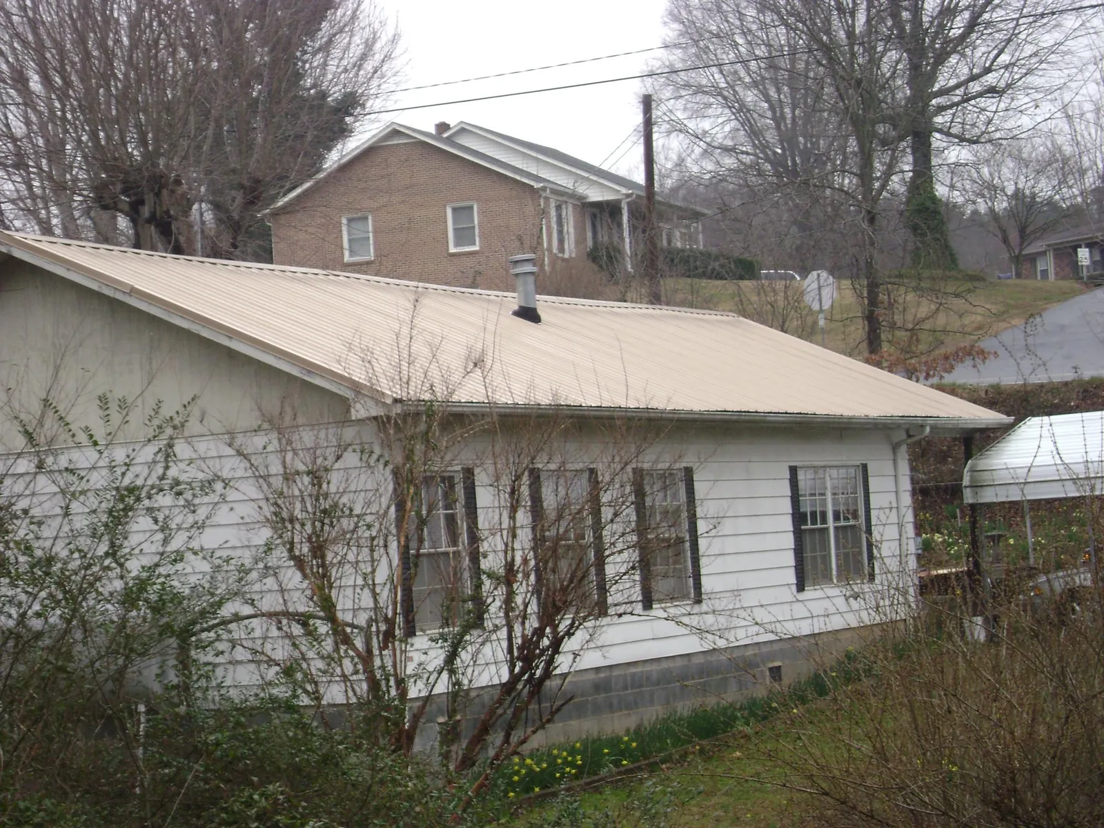 Tan metal roof on a white sided house set into a hillside — Commercial Roofing by Roofing Brothers in Needville