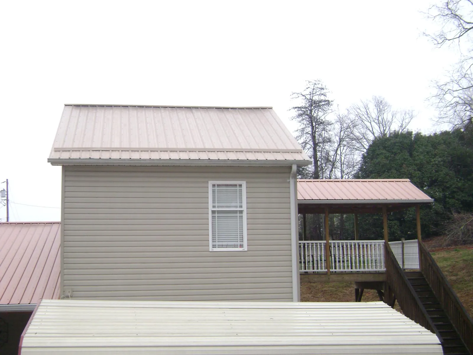Tan metal roofs on a two story addition and attached porch, from a Roof Replacement job in Needville